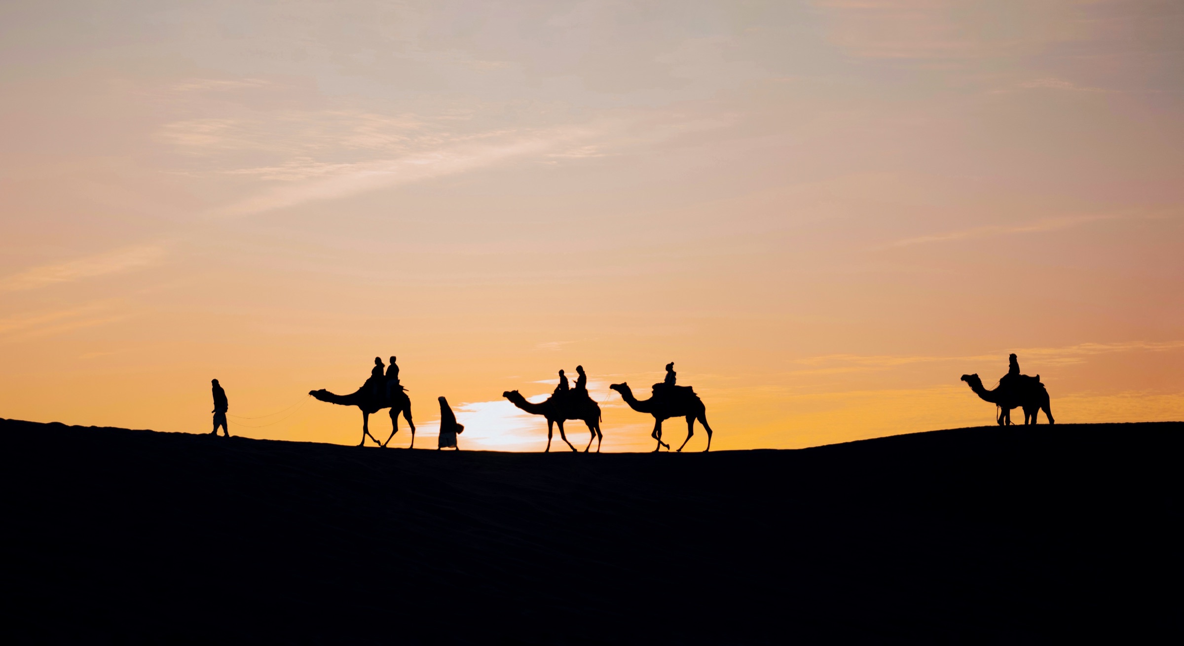 Camel safari silhouettes at sunset in Jaisalmer dunes